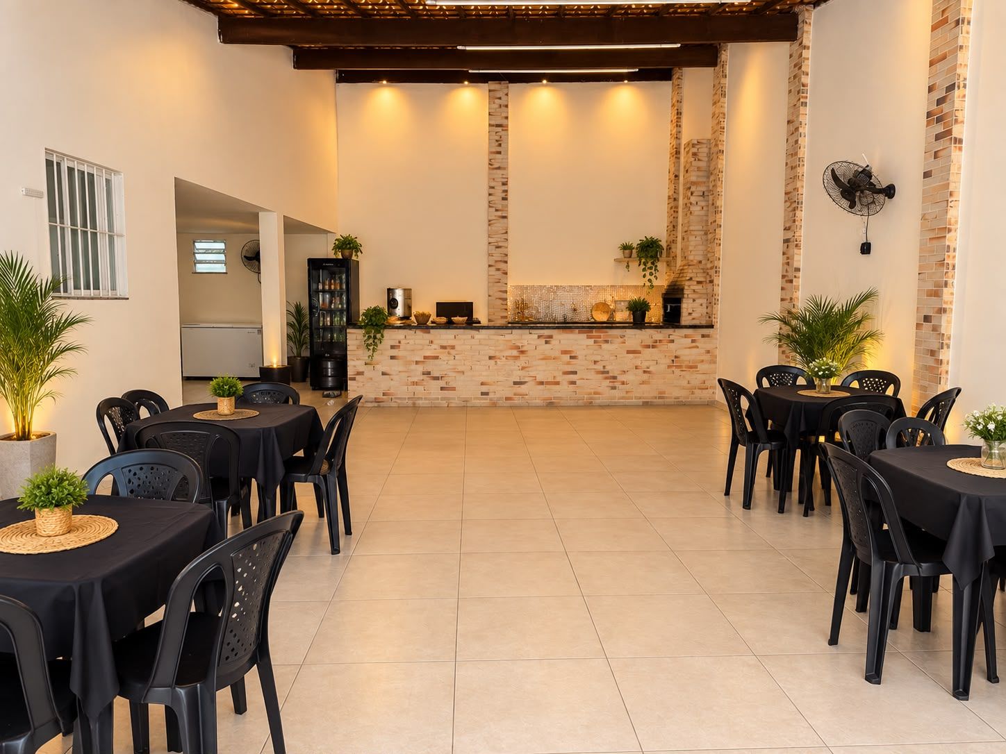 Área coberta com mesas de toalha preta e cadeiras pretas, balcão ao fundo